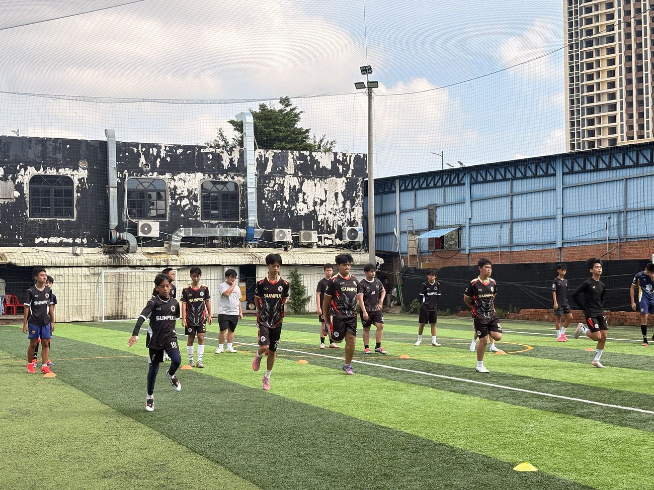Gonner United FC players warming up with high knees on a training pitch, with cones on the grass