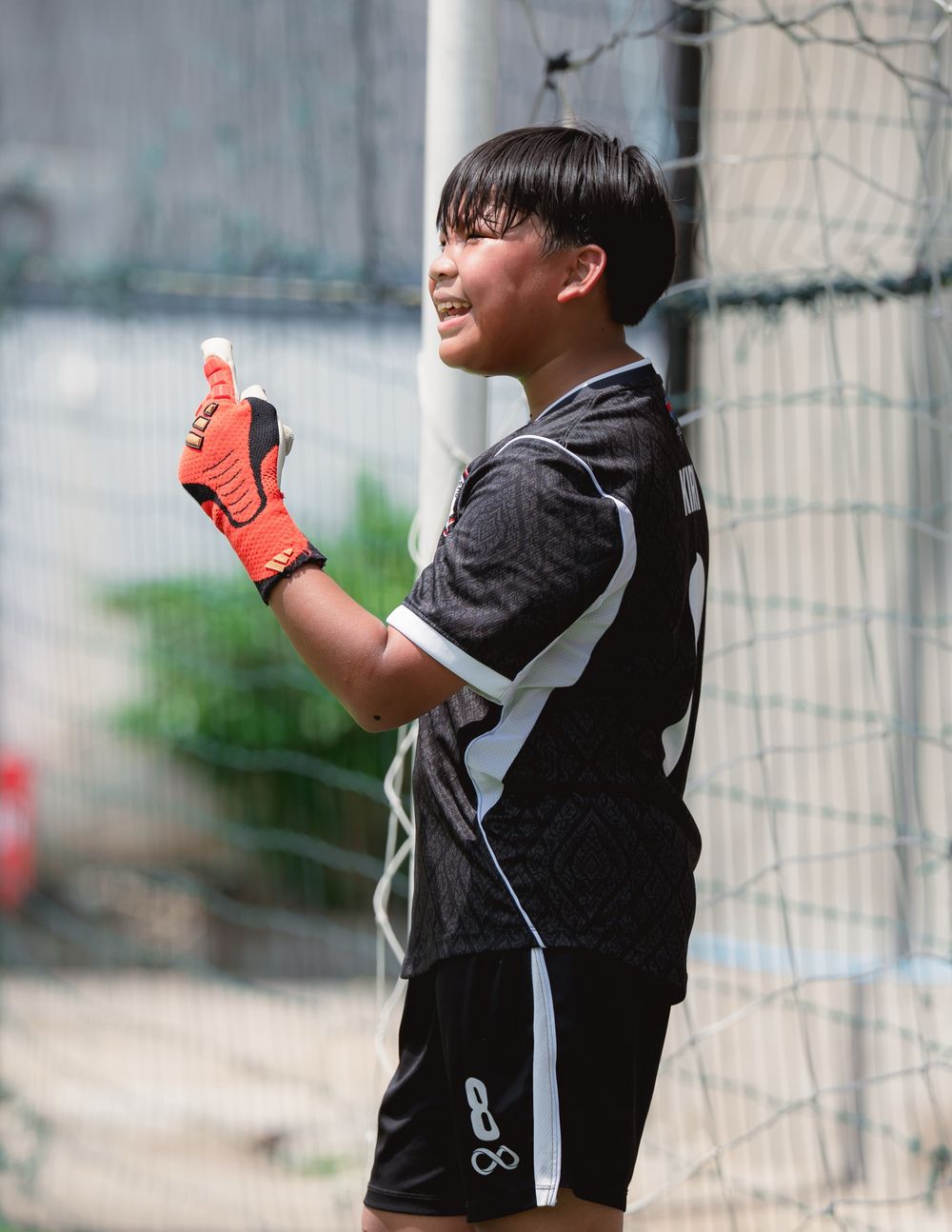 A Gonner United FC goalkeeper in orange gloves gives a thumbs up beside the goalpost
