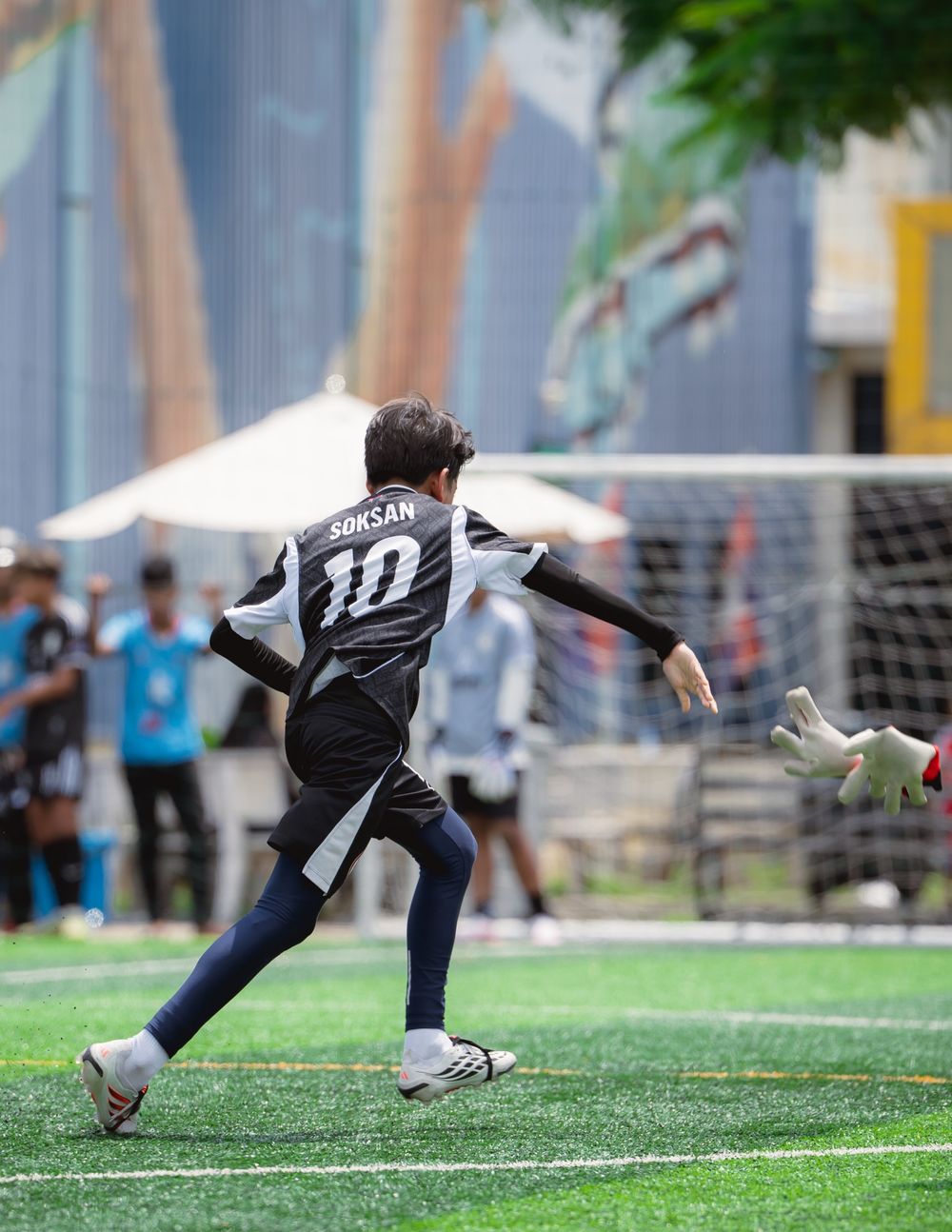 A Gonner United FC player wearing number 10 runs in a match, with a goalkeeper's gloves reaching out beside the goal