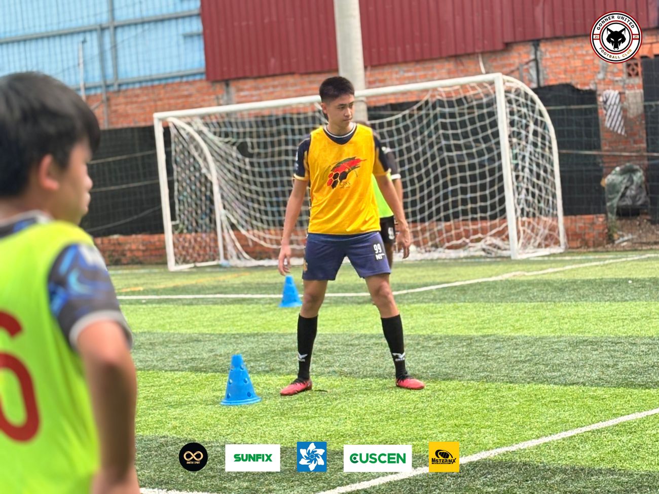 A Gonner United FC player in a yellow training bib stands between two blue cones during a drill