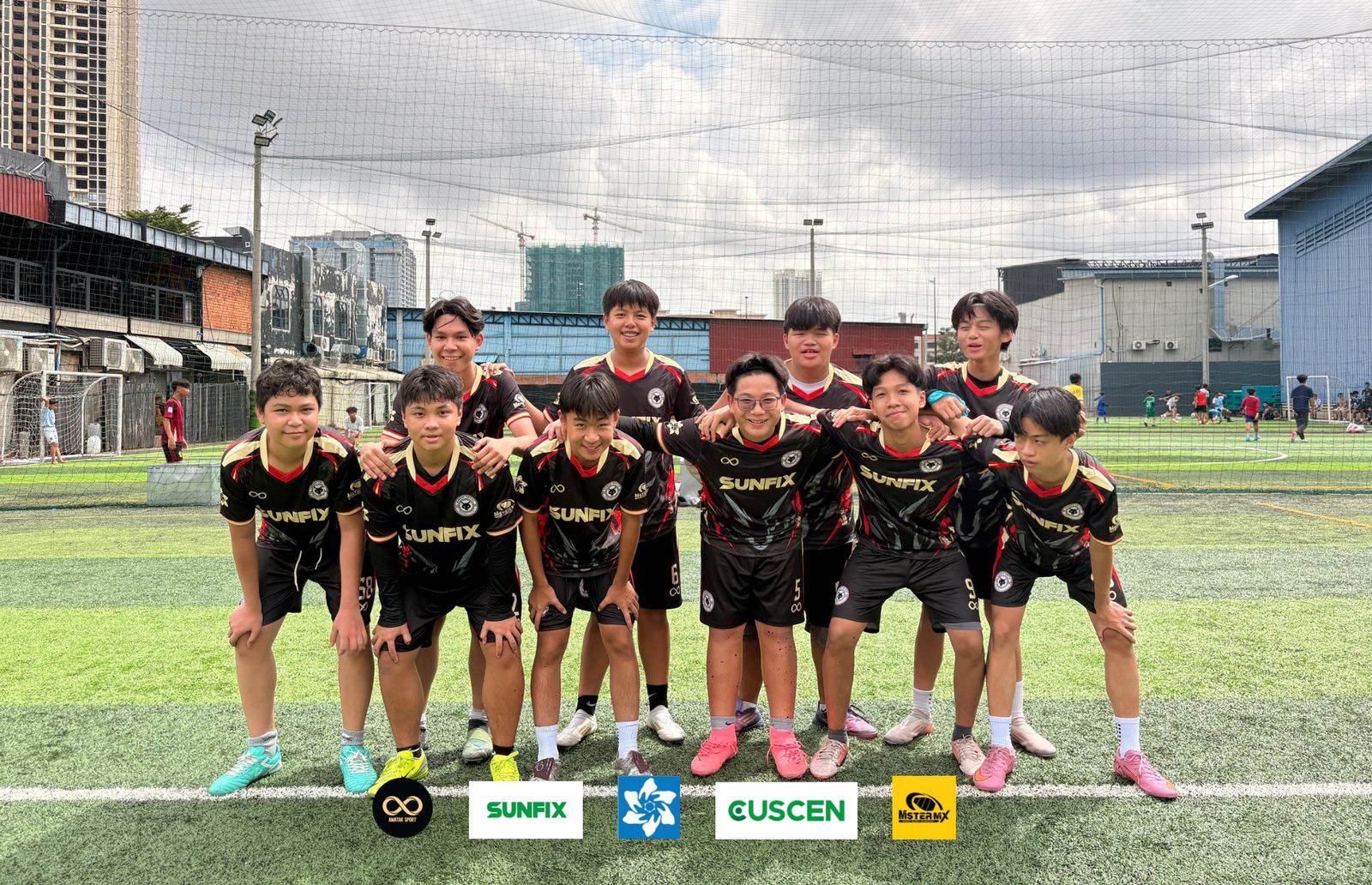The Gonner United FC U16 team in the black, red and gold kit, arms around each other on the pitch